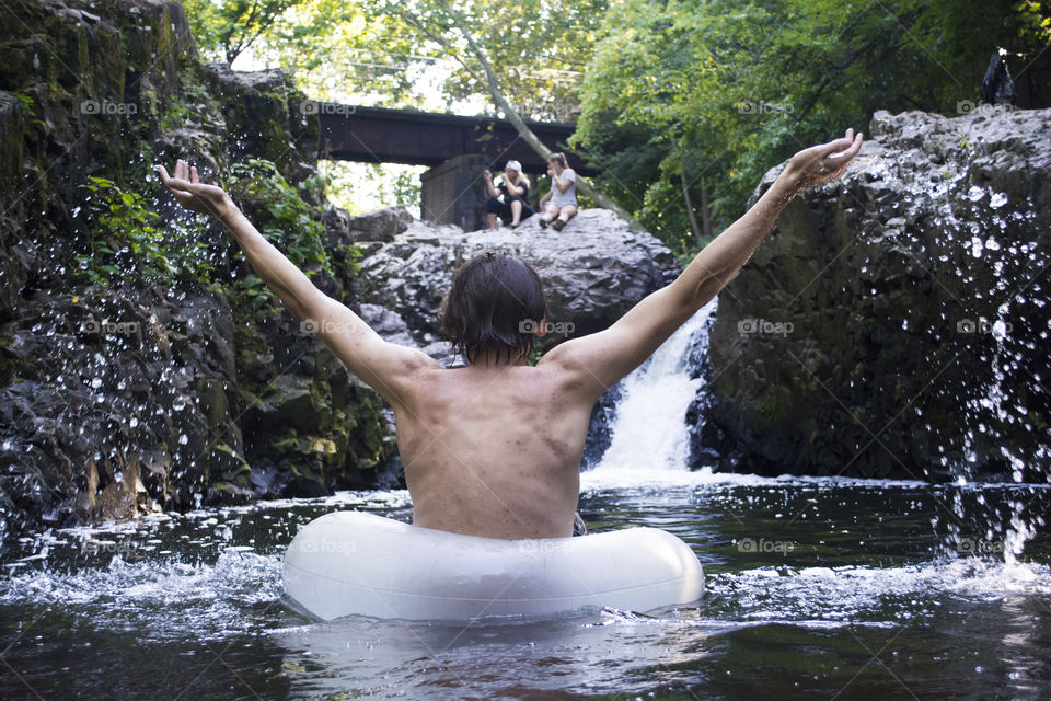 A guy enjoys a natural waterfall in summer as others soak up the sun 