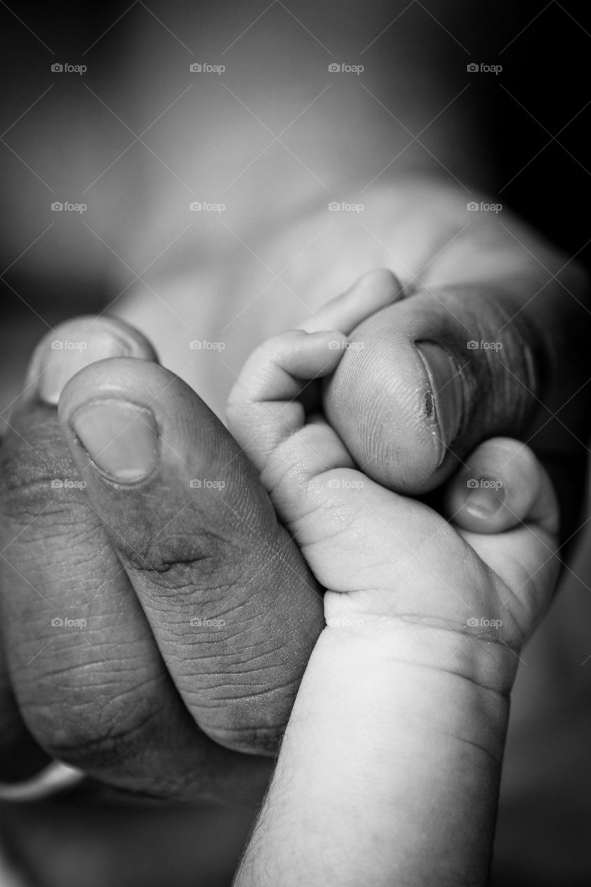Image of working dad's rough hands holding the hand of his newborn baby