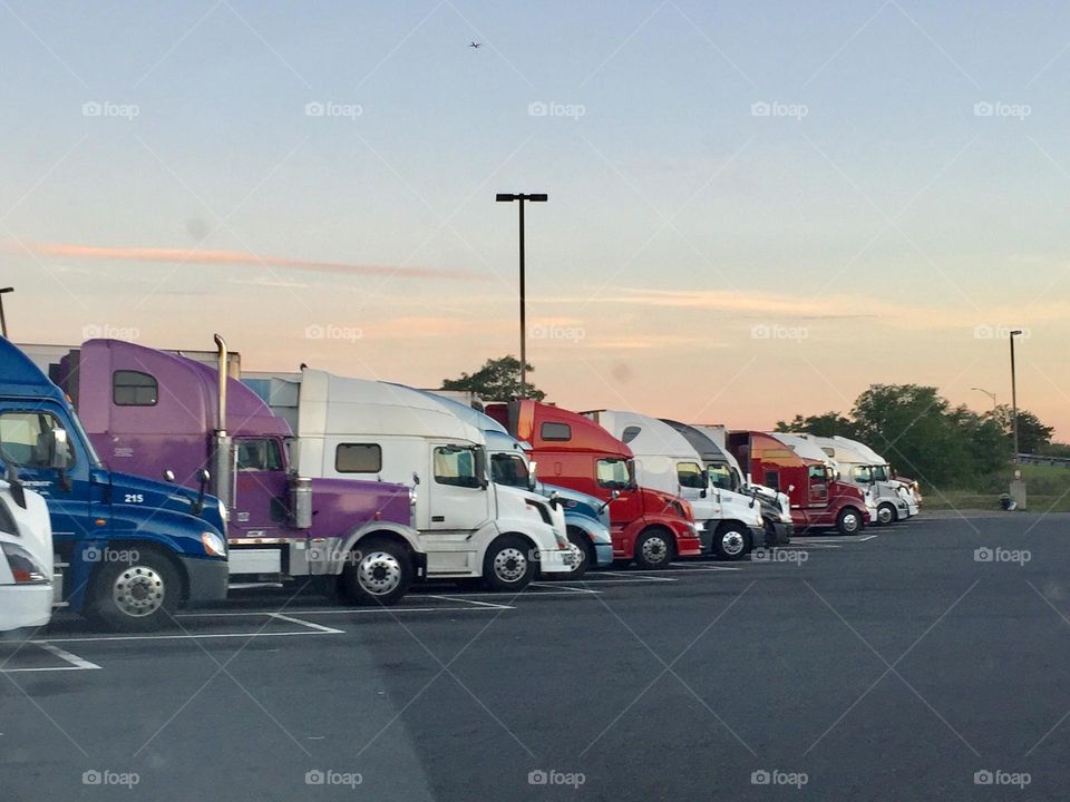 Multiverse - Hail the truck drivers! Long-haul drivers park their 18 wheeler rigs in a row at a truck stop parking lot before driving many more long distances to deliver much needed goods around the country