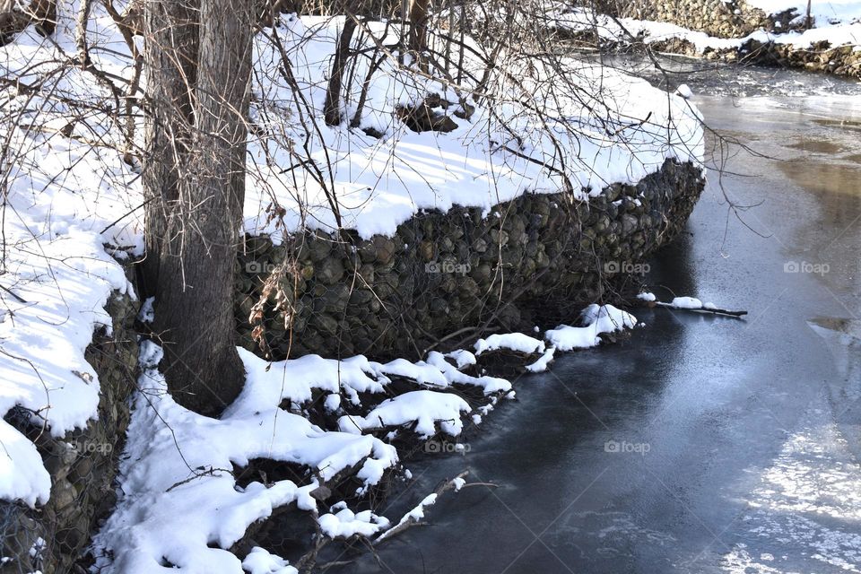 A snowy rock wall overlooking a frigid creek