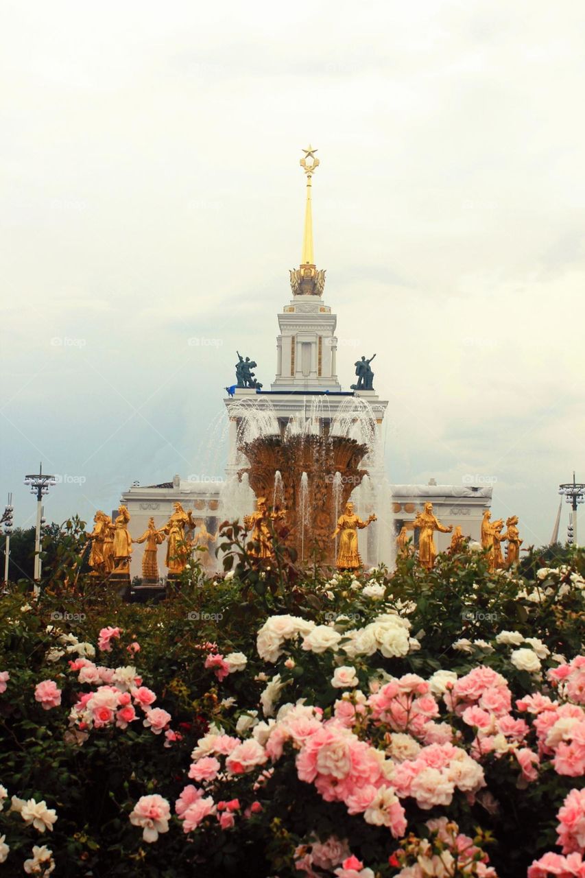 VDNKh in Moscow, Russia. Carnations bloom in spring, cloudy day, golden statues on the fountain, water and soviet architecture, spire