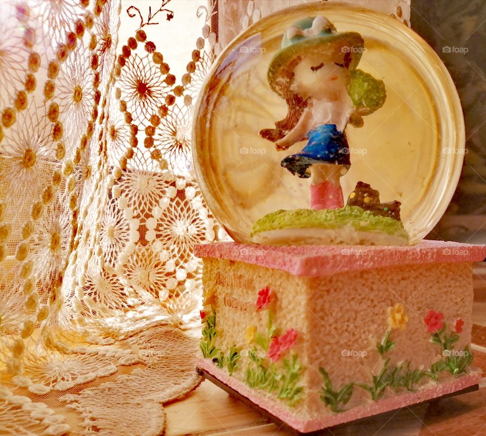 A music box with a snowball in it, a doll in it, a little girl with a curtain that reflects golden sunlight.