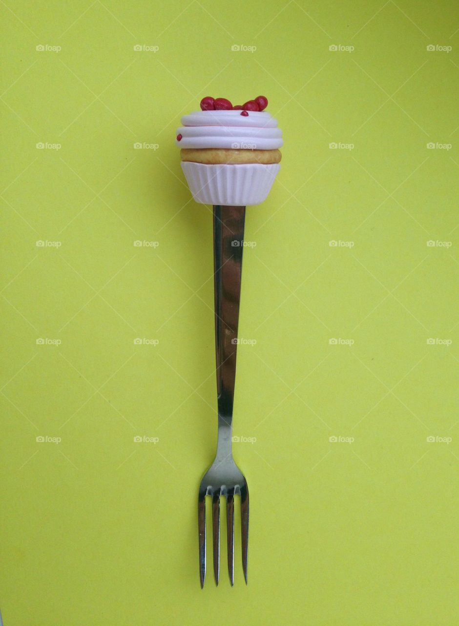 Fork with cupcake on top on yellow background 