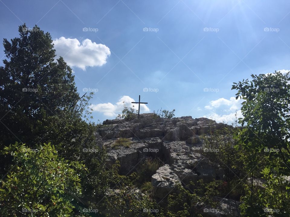 Cross on top of rock against cloudy sky