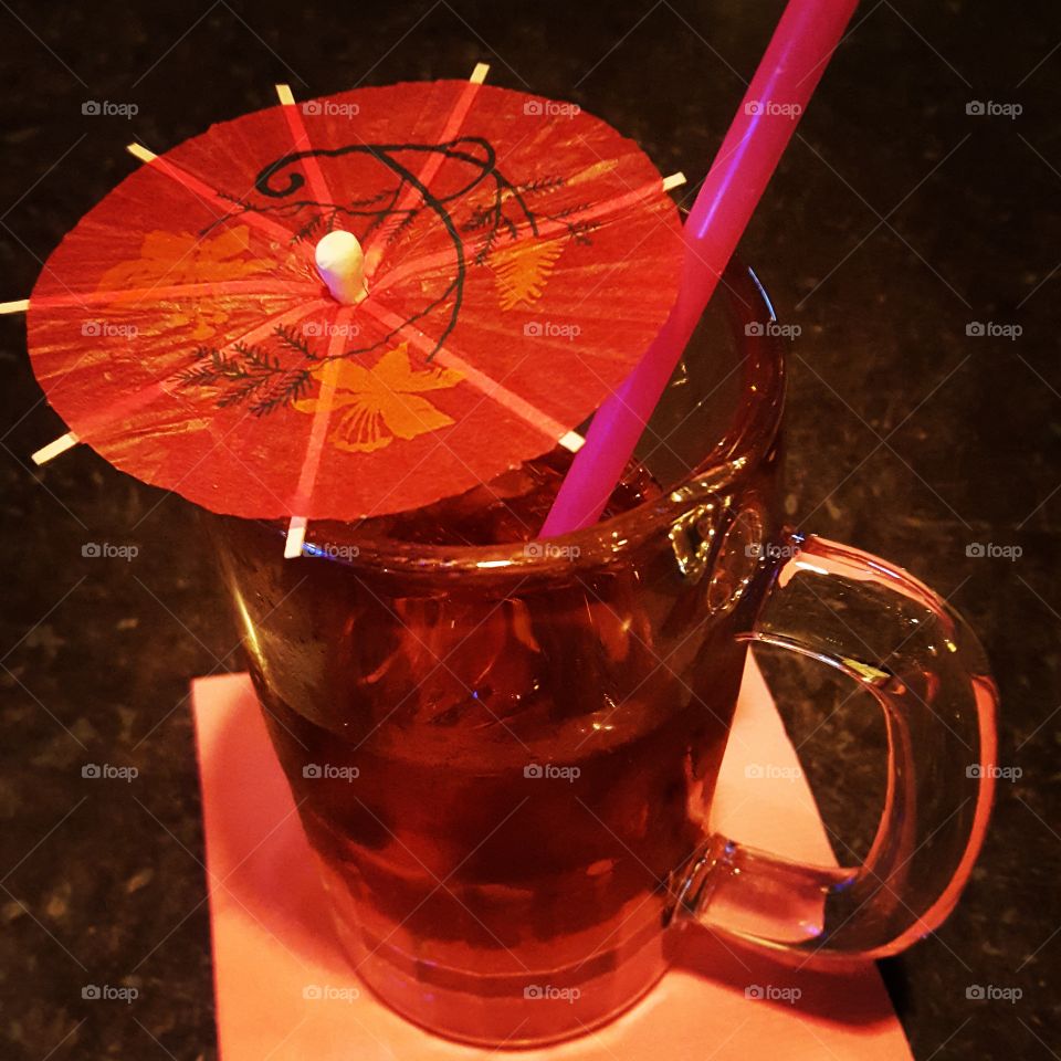 A beverage mug gets elevated from the addition of a bright pink straw and red umbrella.