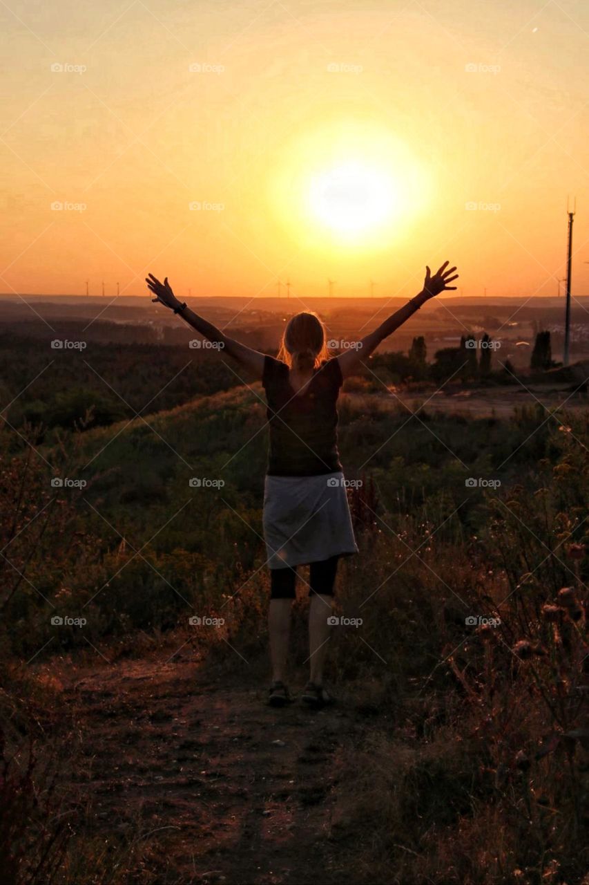 Rear view of a woman stretching her arms in the sky at sunset