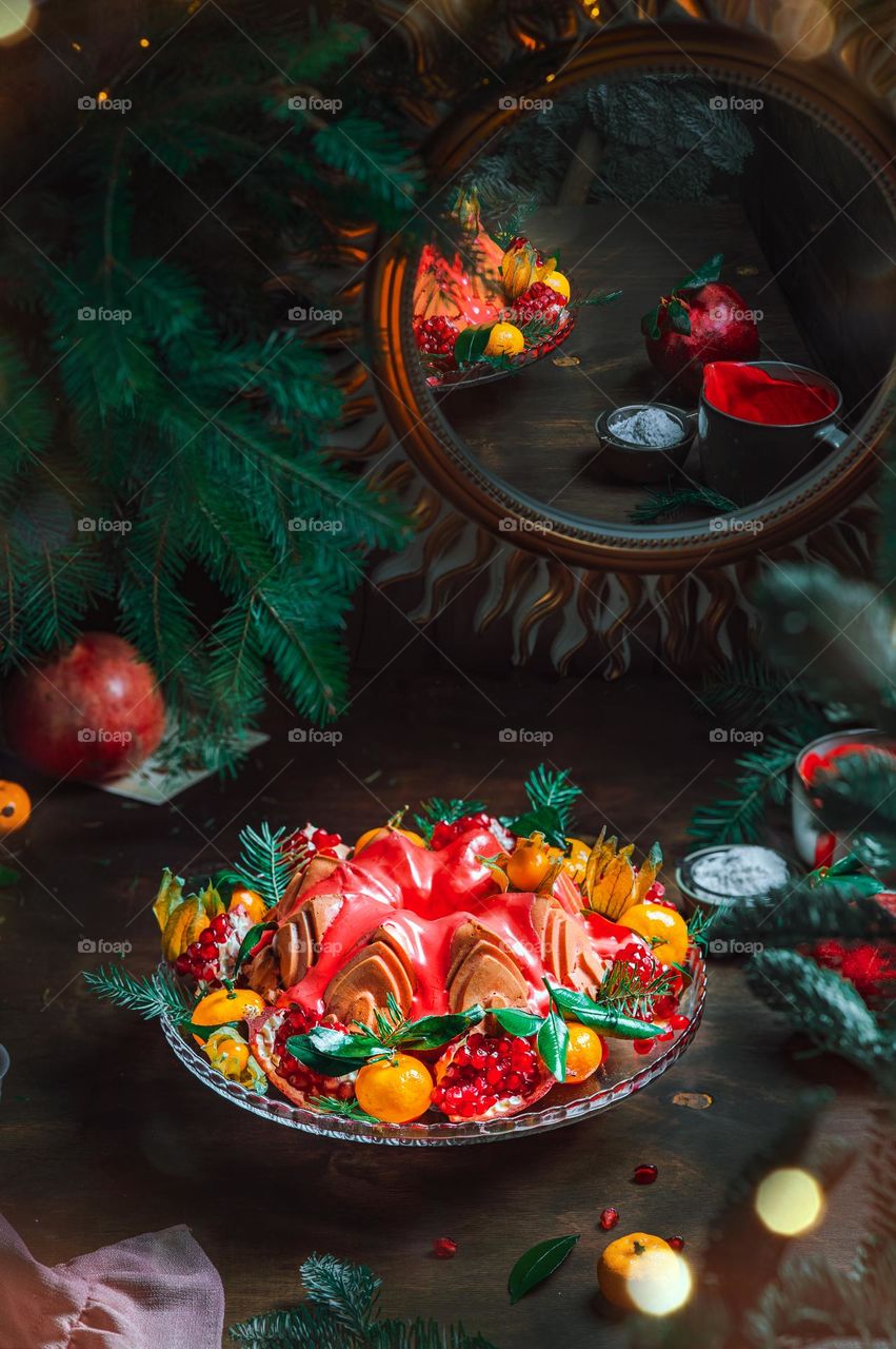 Christmas table setting. Bundt cake pudding sprinkled with sugar powder decorated with pomegranate and tangerines. High quality photo