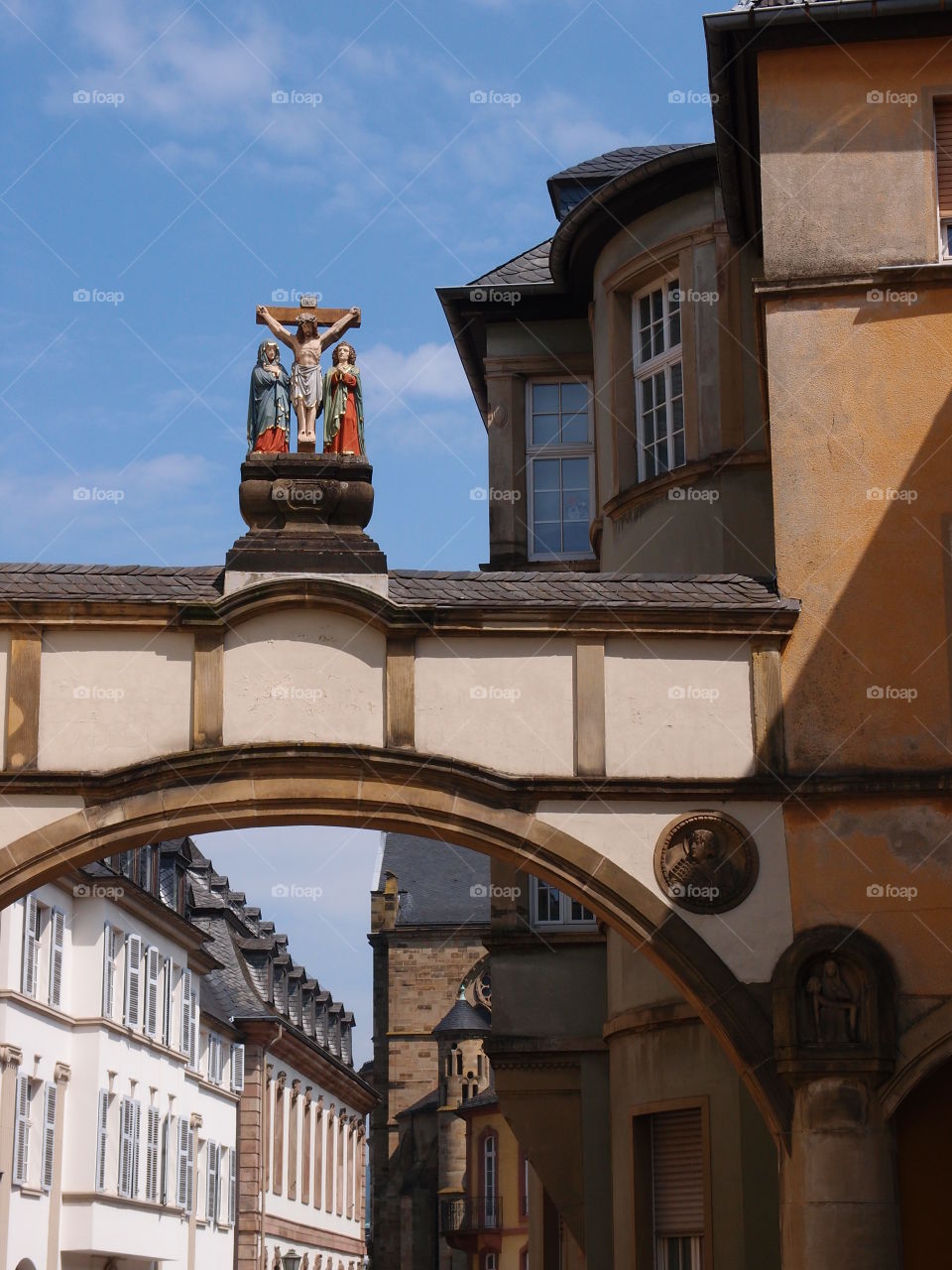 A statue of a crucified Jesus on top of a beautiful arch all against a bright blue sky in Europe on a sunny summer day. 