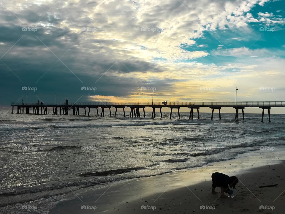 Beach in stormy evening at sunset with pier in background young girl child silhouette on beach foreground