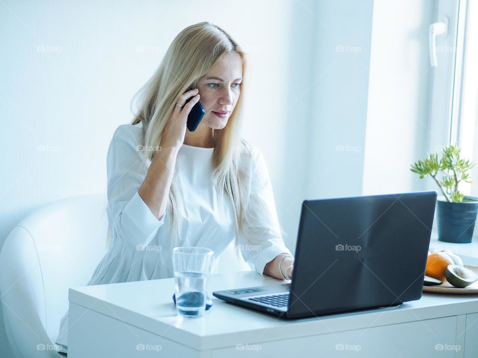 Young beautiful woman in white clothes  with Long blond hair working with laptop and mobile phone 