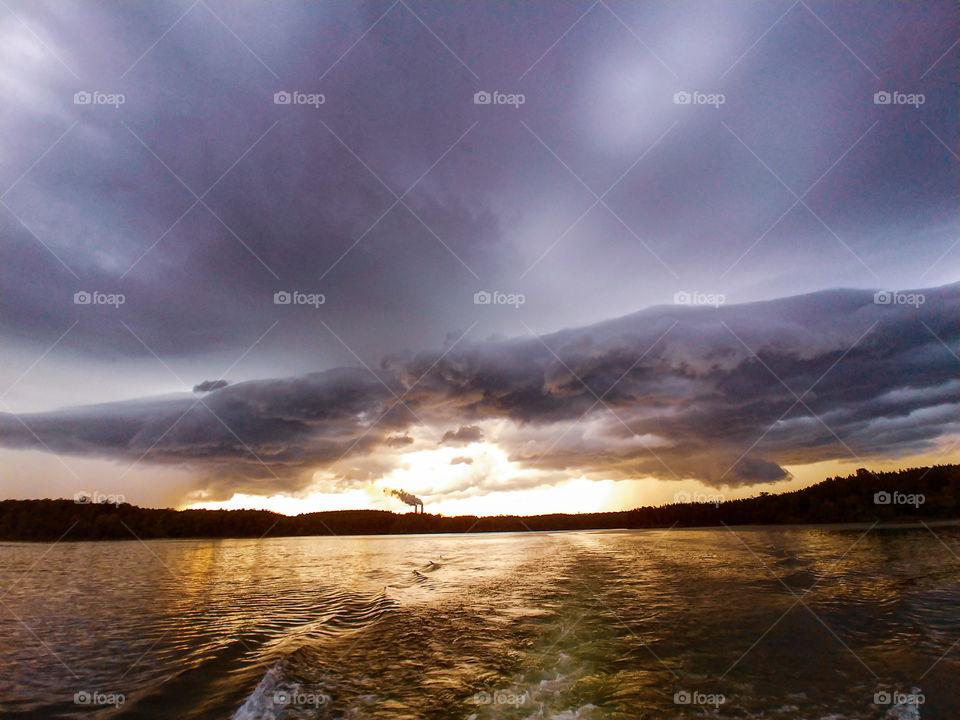 A storm and dark clouds moving in over a lake with steam station in background.