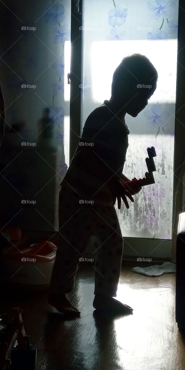 The silhouettes of a boy holding a snake form of blocks that's he assemble and enjoy playing with it.