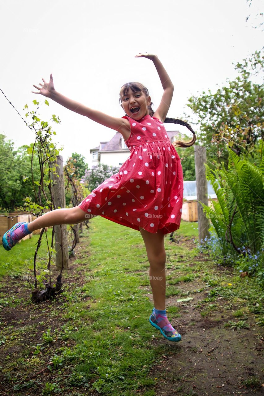 Happy little girl in red dress with white polka dots is jumping high