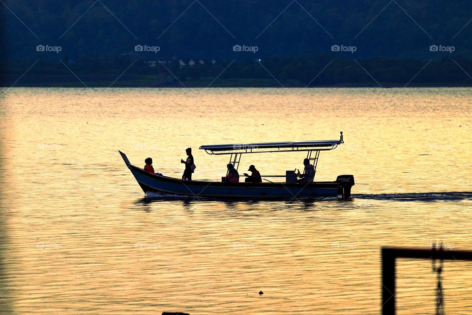 People silhouette on a boat to the other side of the river at sunset