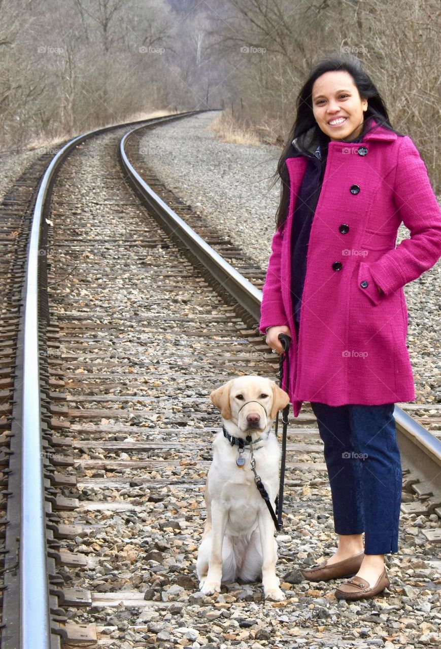 Girl in a magenta coat standing on railroad tracks with a yellow lab