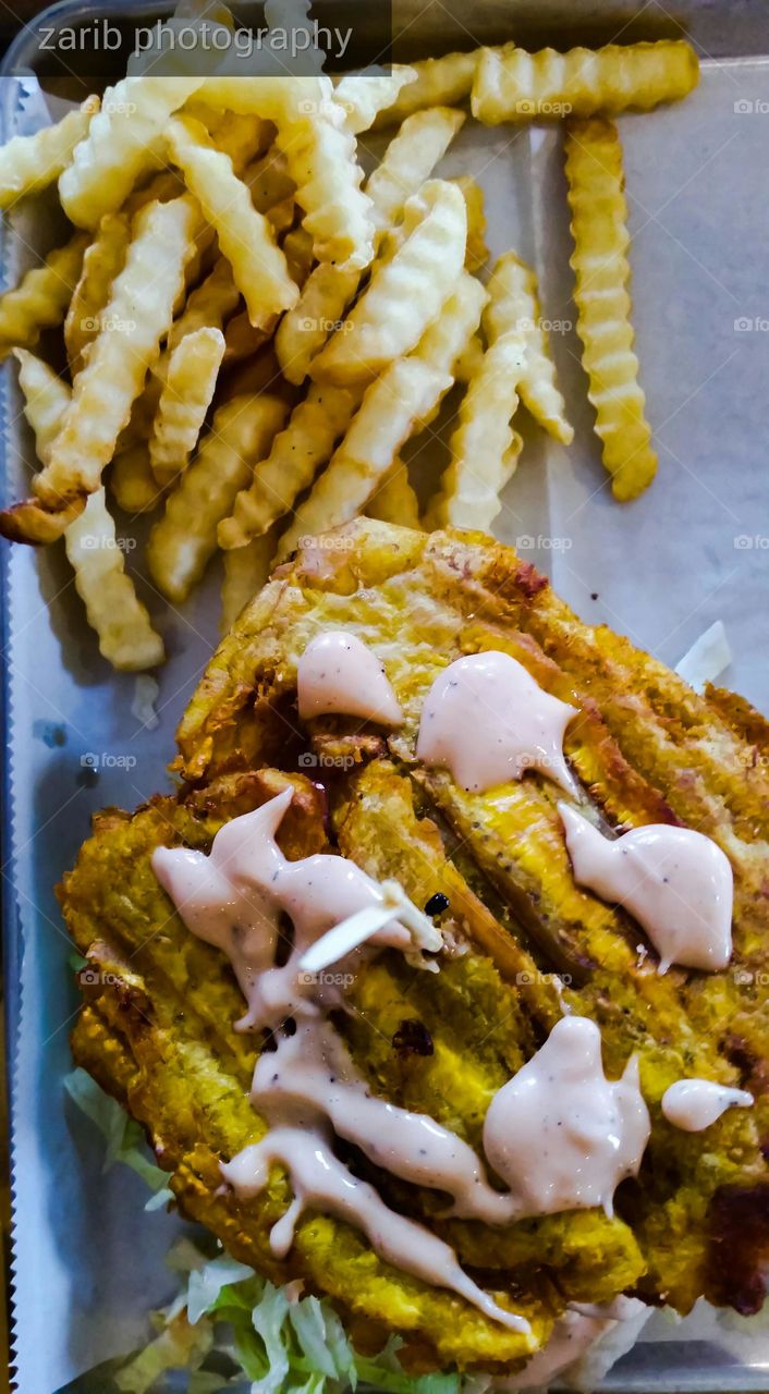french fries complement a plate of plantain filed with meats and lettuce, tomatoes, saute onions with a sauce on top.
