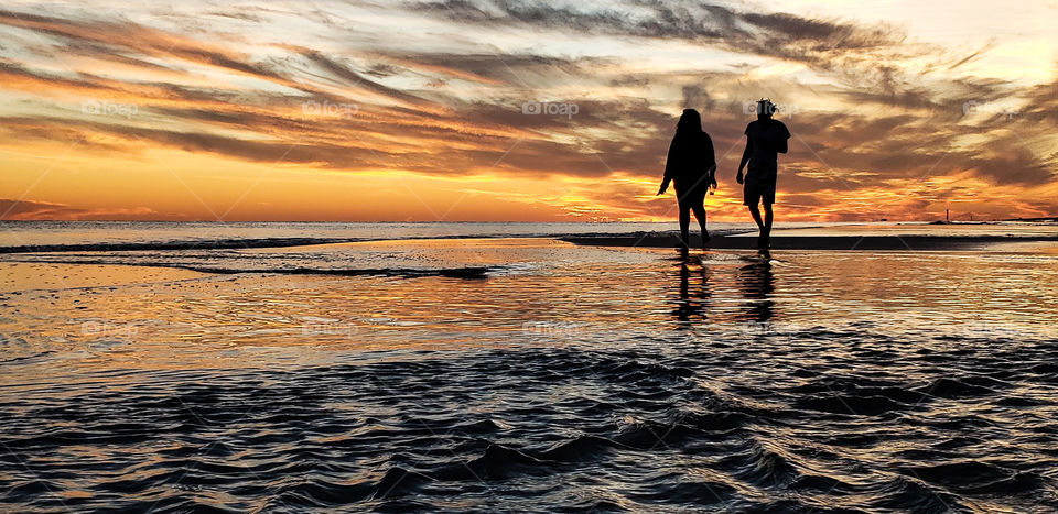 Couple walking in surf at beach during sunset.