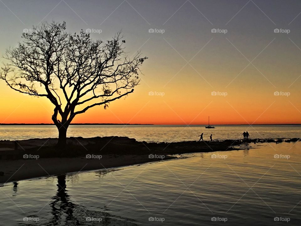 A family walking along the bank of the bay enjoy a fiery orange orb of light slowly sank beneath the horizon, and threads of light lingered in the sky