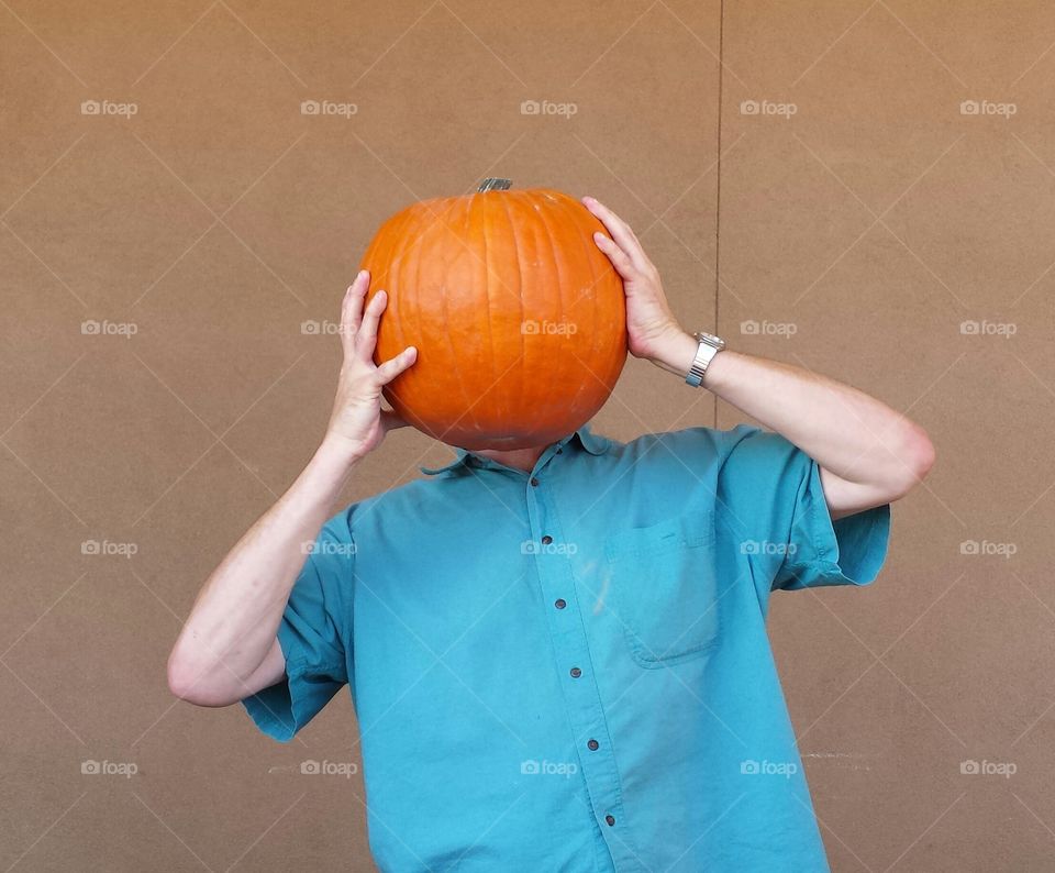 Pum'kin Head 2. Man playfully filling around with pumpkin at grocery store.
