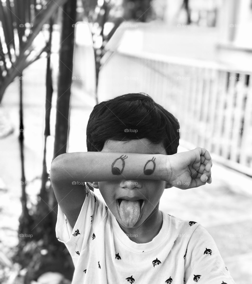 A black and white picture of funny boy showing his tongue out and draw a Mickey eyes on his hand and it’s so funny 