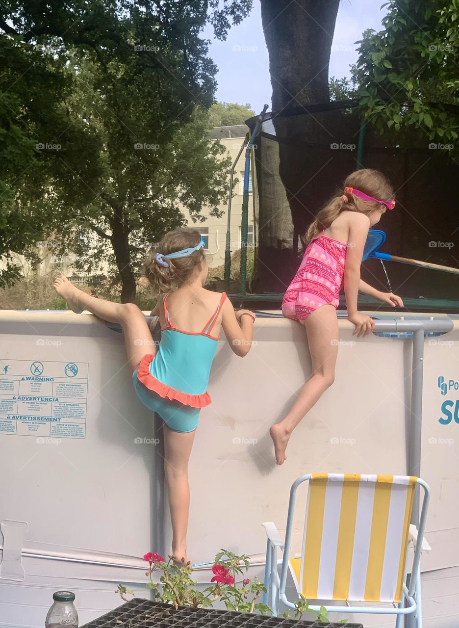 Two girls climbing on home swimming pool with swimming suit and goggles 