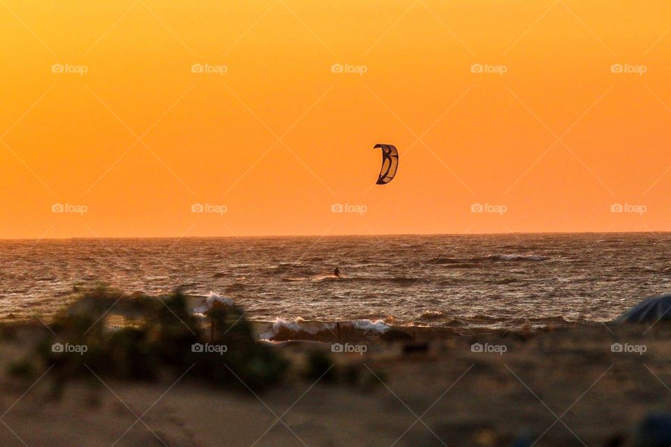 The beautiful orange and golden sunset. And cool breeze pulling the parachute as the wind blows the man is balancing it. The sky glows with vivid colour