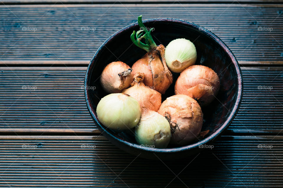 Closeup of bowl of onions sprinkled raindrops on wooden table