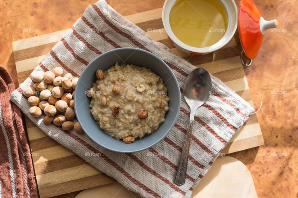 Cooked oatmeal in a deep gray plate with hazelnuts and honey.