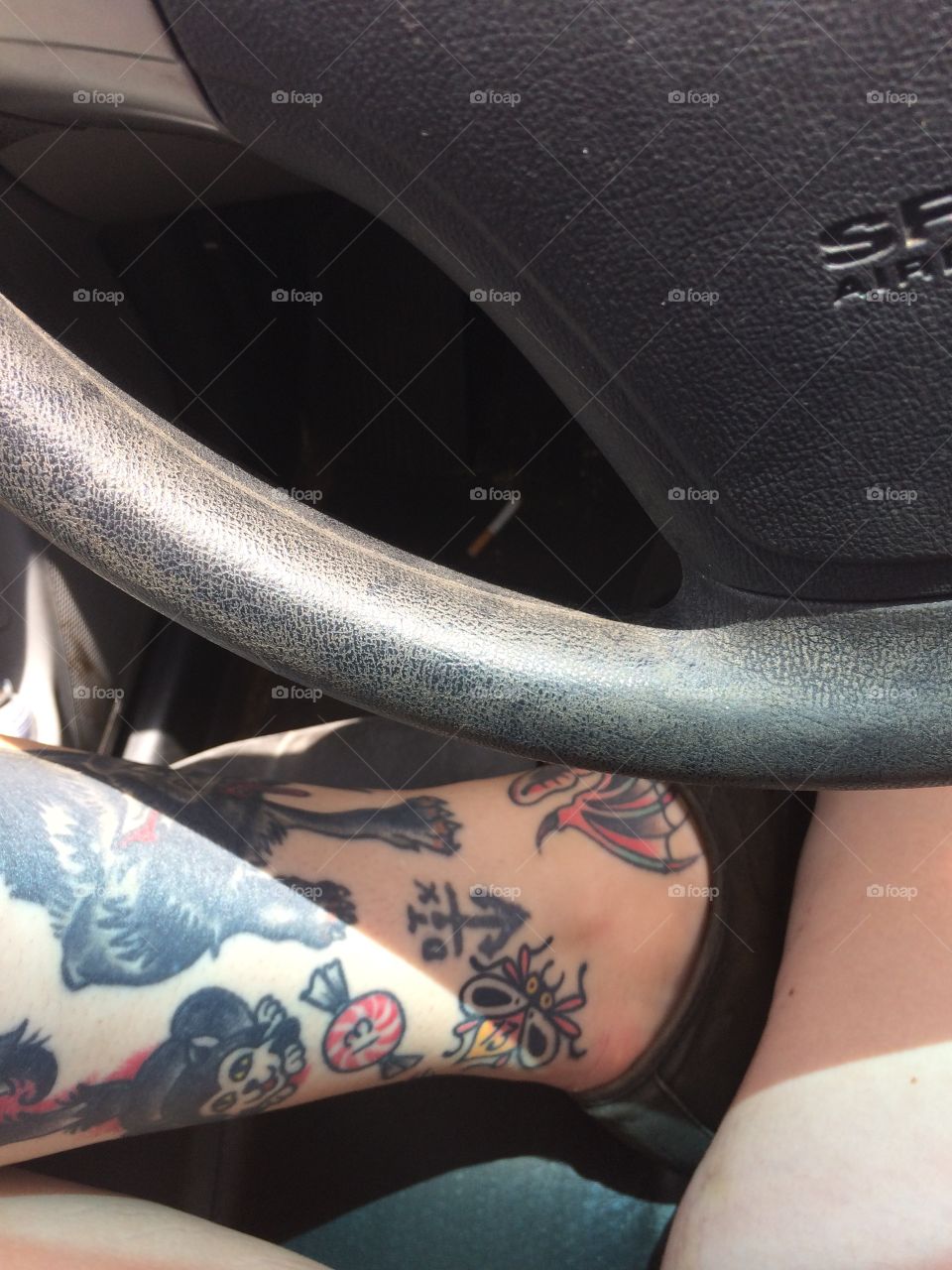 Steering wheel and tattooed ankle. 