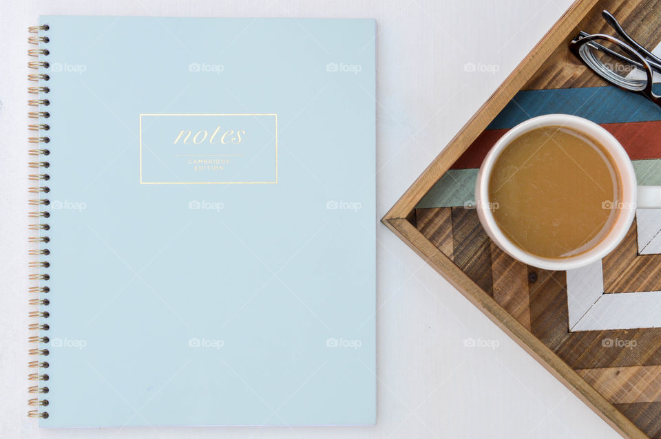 Flat lay of a notebook next to a mug of coffee and glasses on a wooden tray
