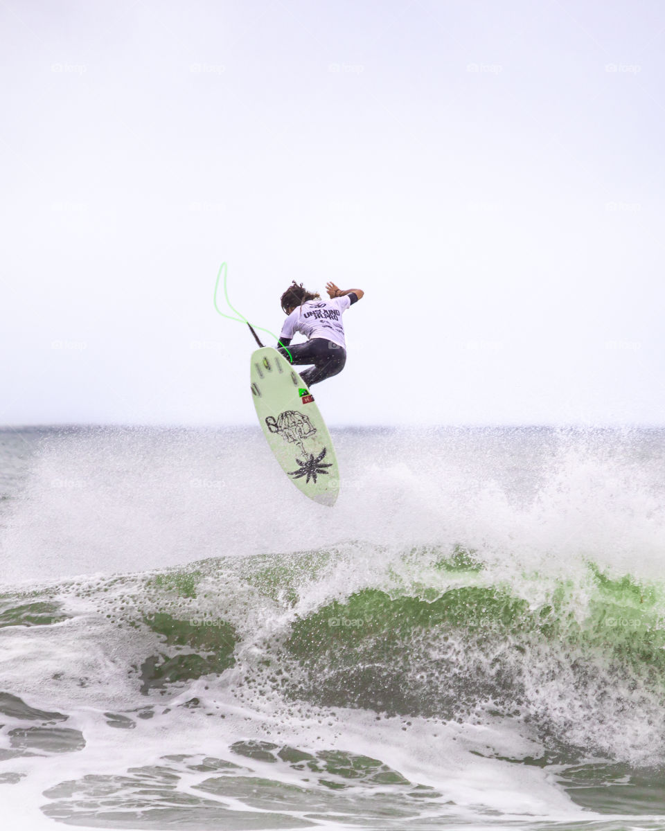 A surfer in the ocean pulling an impressive big aerial trick off of a large wave. 