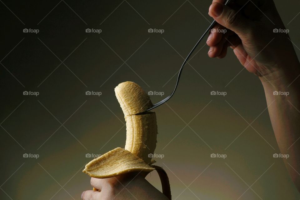 hand sticking a fork to a banana