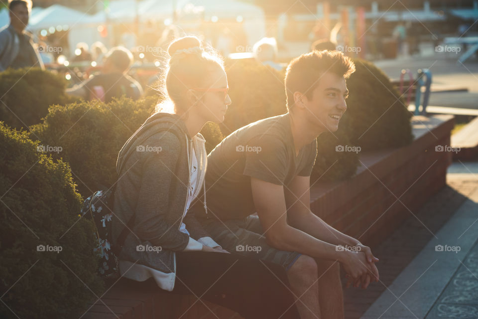 Couple of friends, teenage girl and boy,  having fun together, sitting in center of town, spending time together