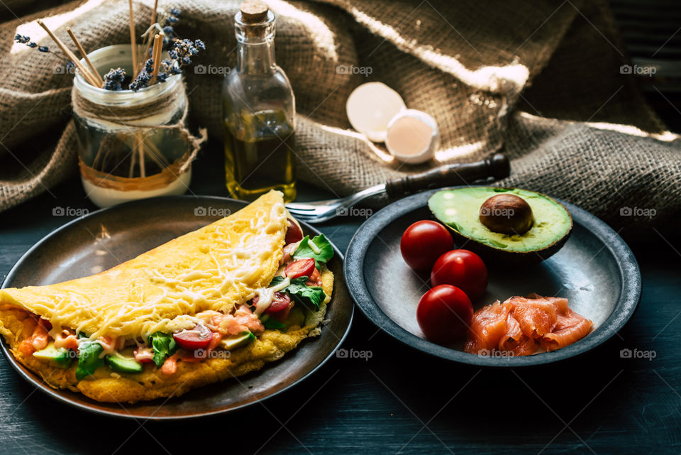 fresh, fluffy omelette with salmon, tomatoes, avocado, cheese and rucola, on a wooden rustic table