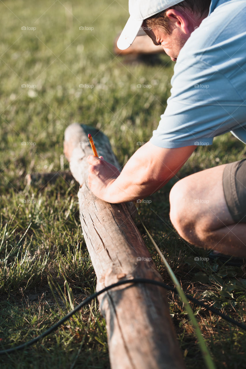 Man making mark by  using pencil after measuring of timber while working in garden