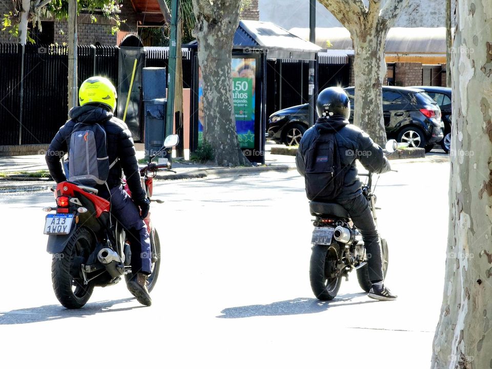 Motorcyclists on two very different types of motorcycles.  One is powerful and big, while the other is cheaper and less expensive. Both are equally versatile in a big city.