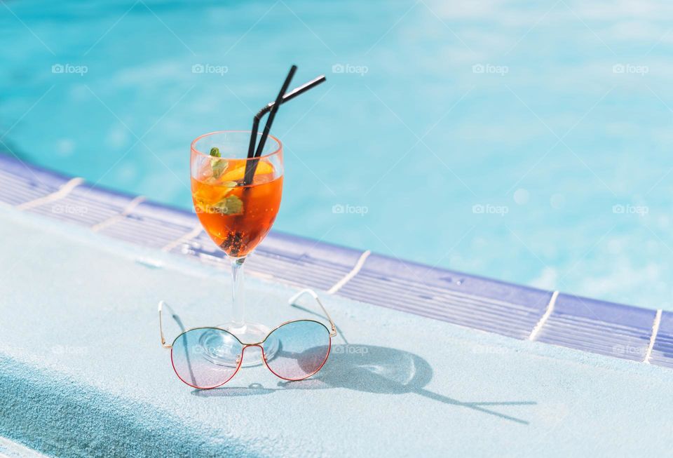 Glass of cocktail with ice and sunglasses on hotel pool, summer vacation