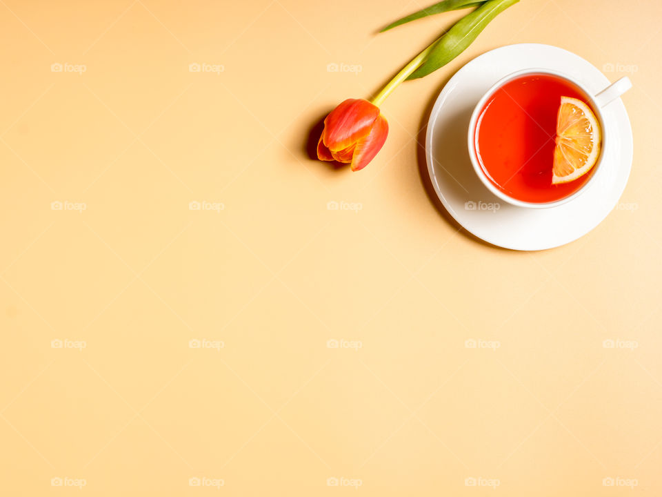 A cup of tea and a red tulip on yellow background 