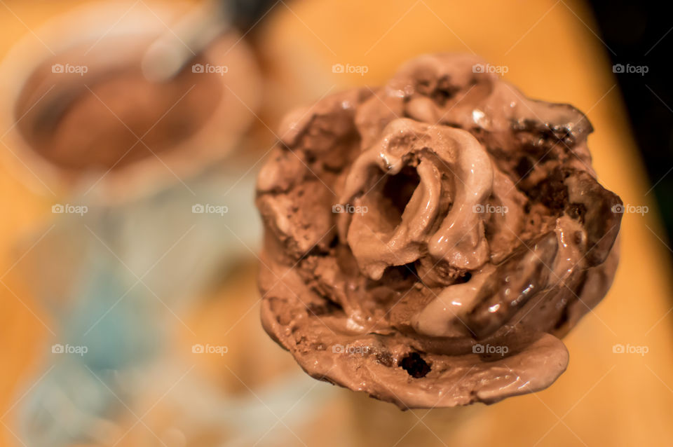 Beautiful chocolate ice cream cone with ice cream rose, heart shaped center and brownie pieces on wood table with tub of ice cream in background for National Chocolate Ice Cream Day gourmet dessert 