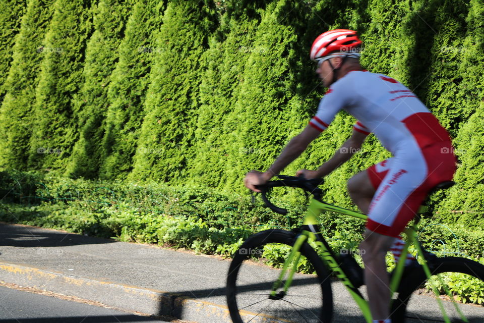 Biker speeding on the road against the green hedge 