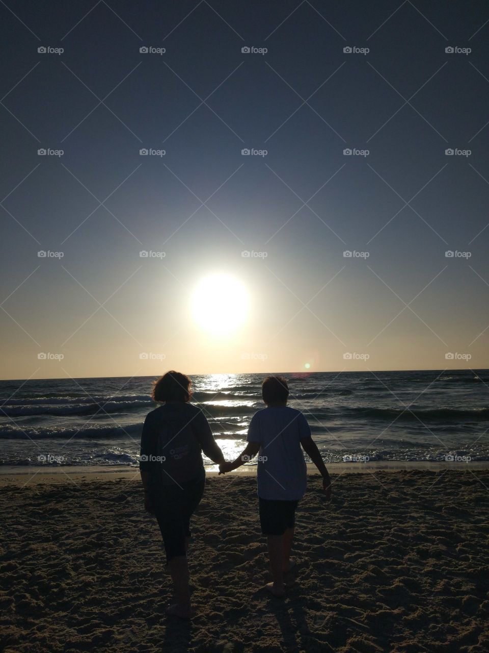 Mom and son walk on the seashore at sunset.
