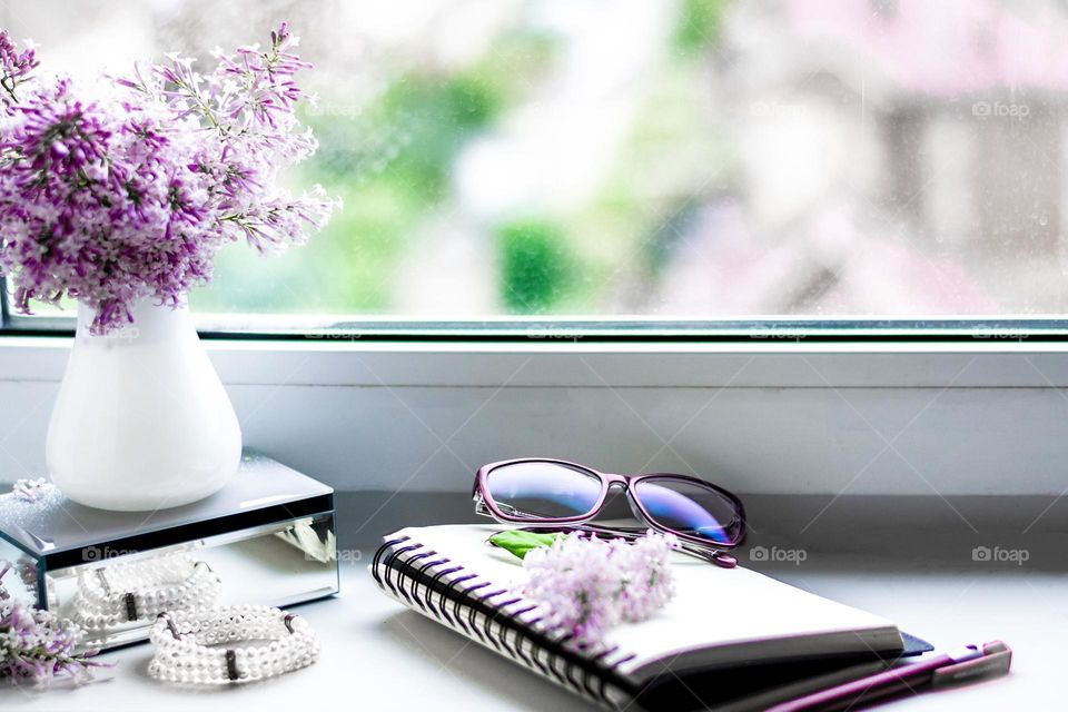 Still life with lilac flowers on the window, glasses and a notepad