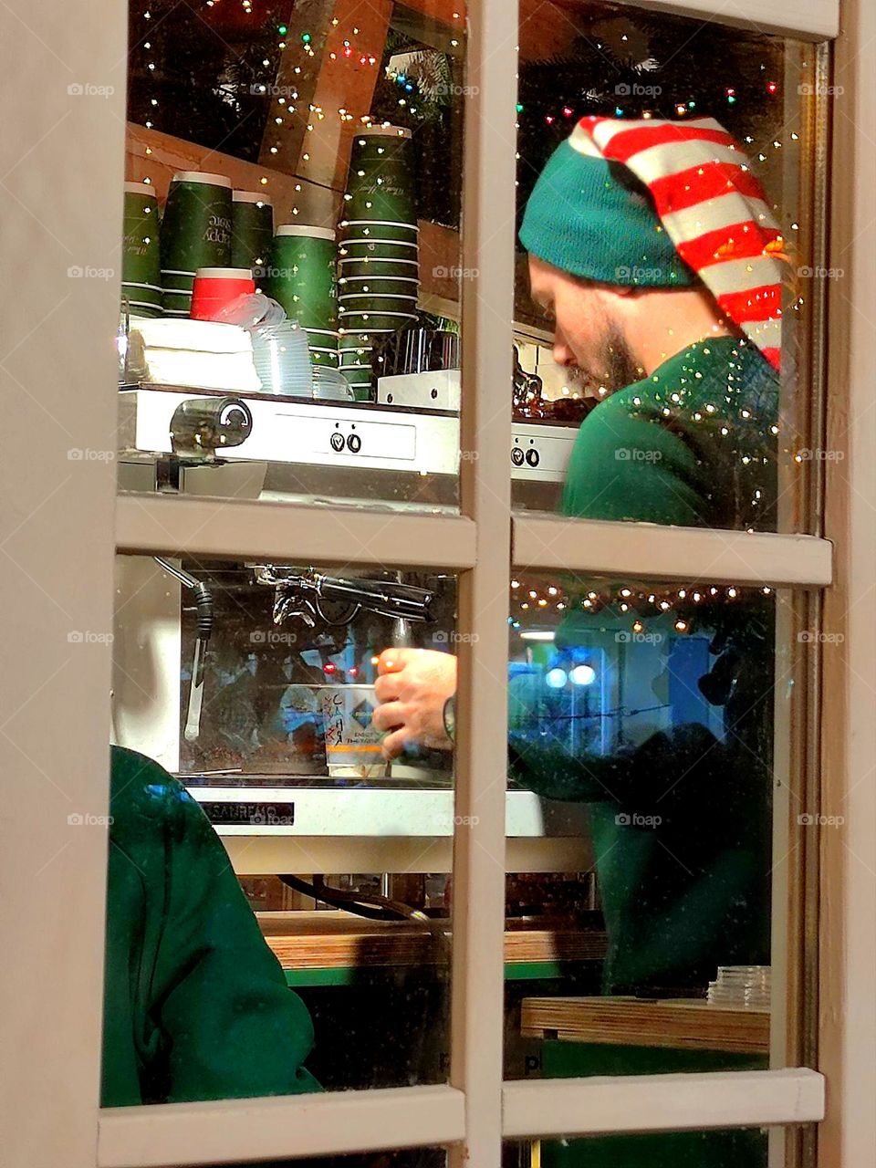 Window of an evening cafe. A man dressed as an elf makes coffee