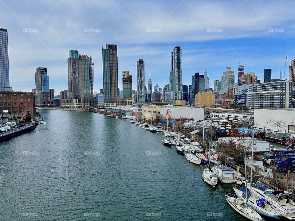 This is “Newtown Creek” with its many boats seen from the “Pulaski Bridge” that connects “Greenpoint”, Brooklyn to LIC, Queens. In the distance across the waters of the “East River” we see “Manhattan”. 2024. Hypnotic Productions
