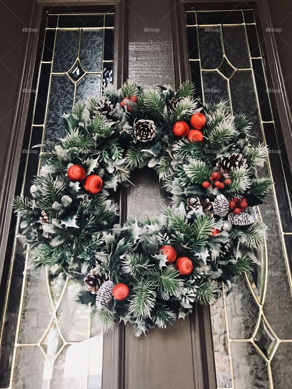 A holiday green Christmas wreath with holly berries and red bulbs on the front door on a cool crisp day 