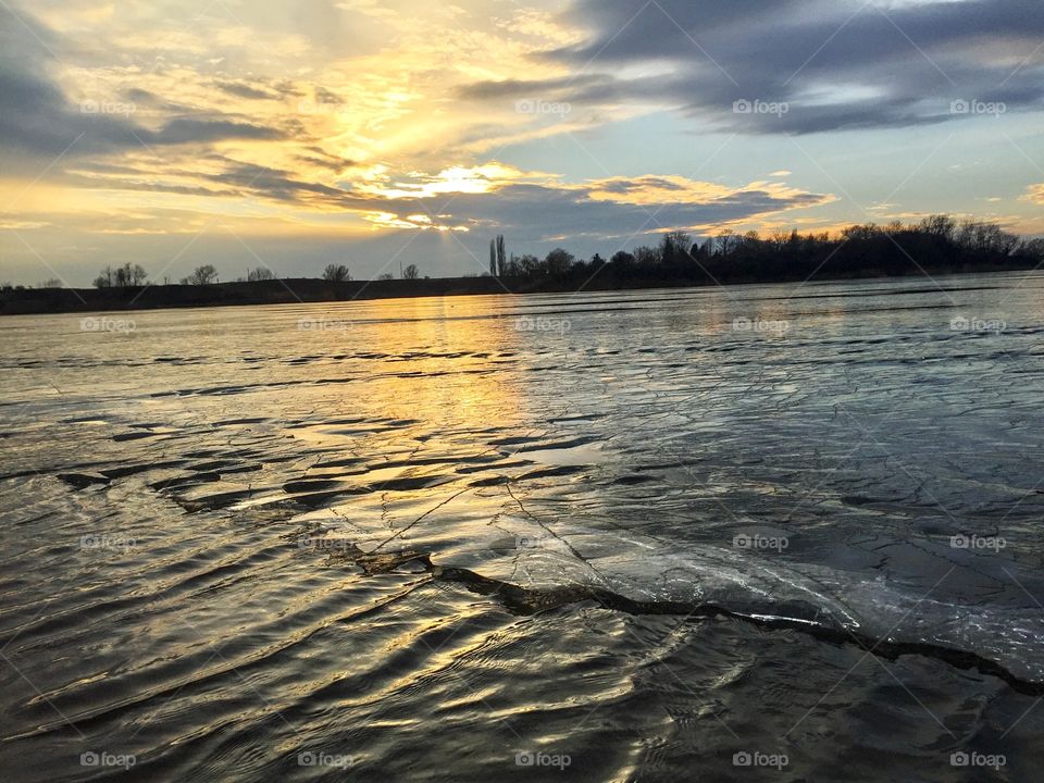 Frozen lake starting to defrost at sunset