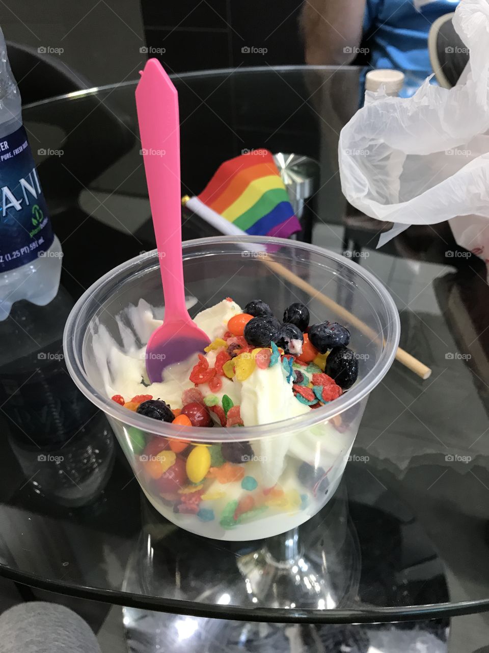 White frozen yogurt full of rainbow Skittles and cereal, with a pink spoon and Pride flag