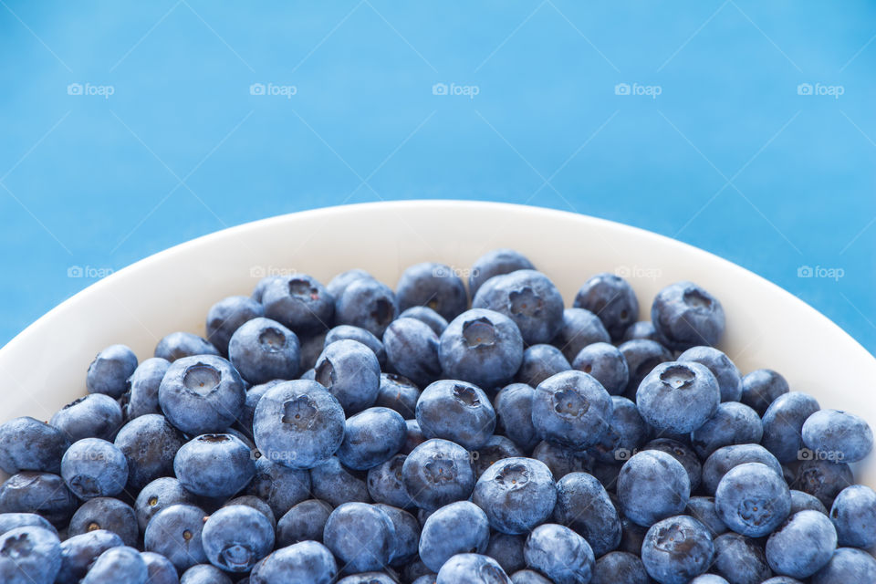 White bowl full of blueberries with blue background. Can be used for summer, food, nutrition, healthy, lifestyle, fresh themes
