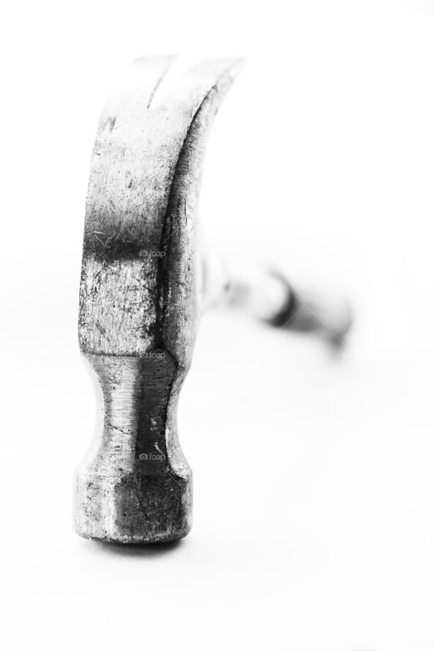 A black and white art portrait of a claw hammer standing upright on the hammer part. the claw is pointed up.
