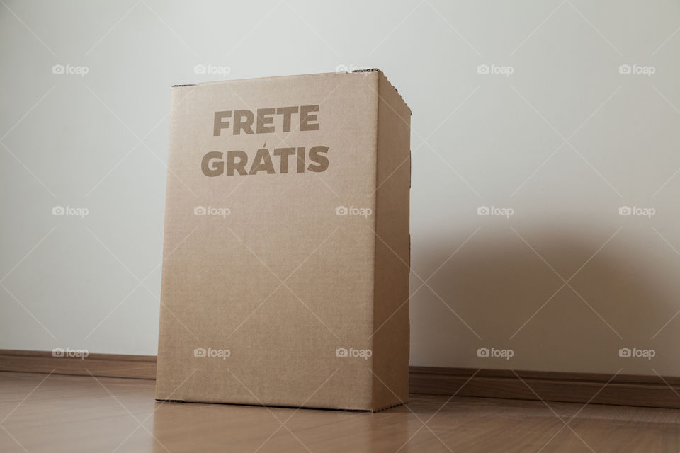 Detail of man with black gloves holding a cardboard box written free shipping to deliver products on gray background. Delivery concept. Delivery service concept. Copy space. Black friday concept.